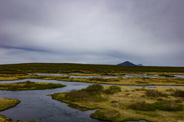 Icelandic valley with flowing river. Mountain range on the horizon.