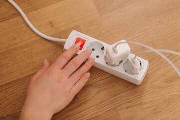 Top view of female hand turn on the extension cord at home. White cable connector