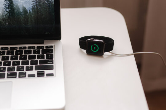 Smart watch on wireless charging with on-screen charging indicator. Work place near at the laptop