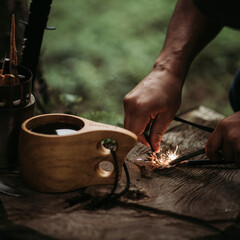 Man´s hand sparkling a ferro rod with a wooden cup with coffee