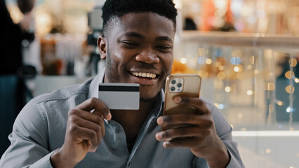 Satisfied african american man makes purchase in online store pays for goods with credit card on...