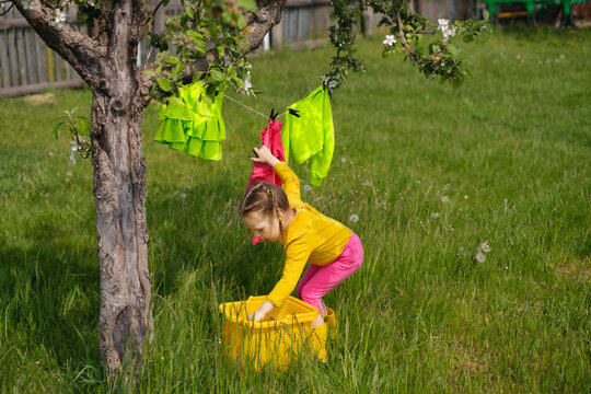 Girl hangs wet laundered clothes on a clothesline under tree in the garden. Washing detergents for colored laundry. Preservation of the brightness of the juiciness of the color of fabrics when washing