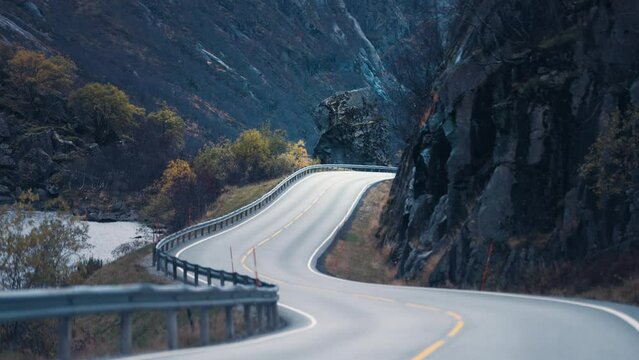 Two-lane country road winds between the steep rocky slopes. Slow-motion, pan forward.