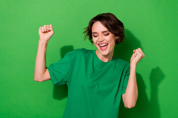 Photo of lucky funny young lady dressed casual t-shirt smiling rising fists isolated green color...