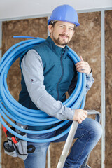 male tradesman with reel of blue pipe on his shoulder