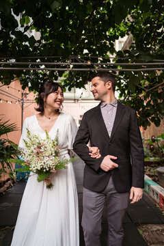 Happy diverse newlyweds with bouquet of flowers in garden
