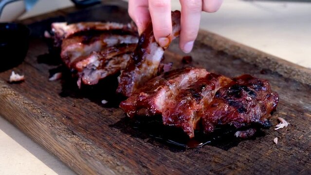 Tasty and delicious barbeque pork ribs grilled, fried outside, outdoor, on wood charcoal grill. national barbeque day. street food. BBQ cooking. An unrecognizable woman takes a piece and eats.