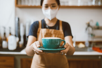 Barista Asian women standing behind the counter and holding coffee cup for offer to customer. coffee preparation and service concept. small business, startup business.