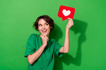 Photo of charming dreamy woman wear casual t-shirt arm chin looking heart like sign empty space isolated green color background
