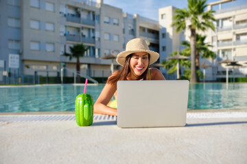 digital nomad woman working remotely online in a swimsuit with long black hair and a laptop in a swimming pool
