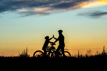Obraz na płótnie Canvas Silhouette of happy father and son biking at sunset