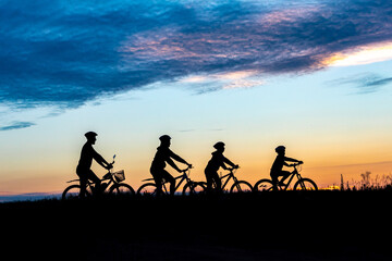 Fototapeta na wymiar parents and kids ride bicycle at sunset. family on cycle ride in countryside. Silhouette of cyclist