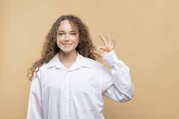 Happy Girl with curly hair shows ok gesture on beige background