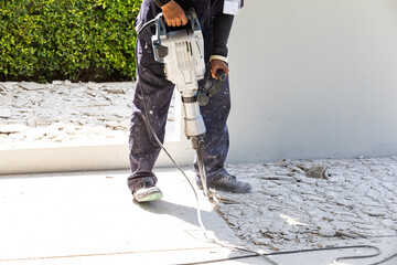 Builder worker with pneumatic hammer drill equipment breaking concrete at floor