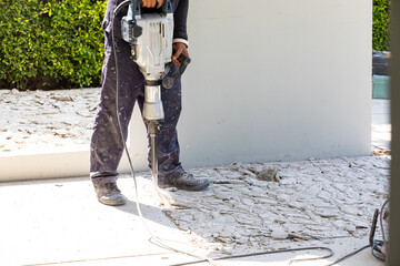 Builder worker with pneumatic hammer drill equipment breaking concrete at floor