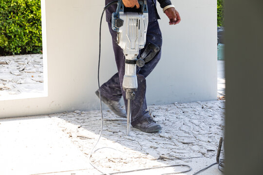 Builder worker with pneumatic hammer drill equipment breaking concrete at floor
