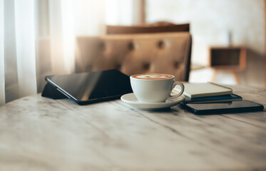 Close up view, white coffee cup with tablet computer, smartphone and notebook on table, relax after work in cafe, vintage color tone and soft light from window on background