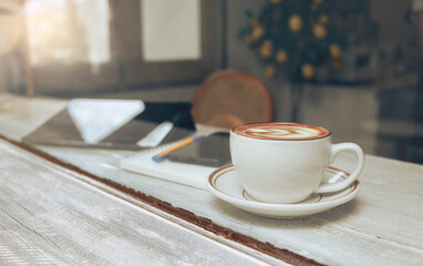Close up view, latte coffee in ceramic cup with mobile phone and pen on note book on wooden table, relax in cafe after work, Retro stly and vintage color tone