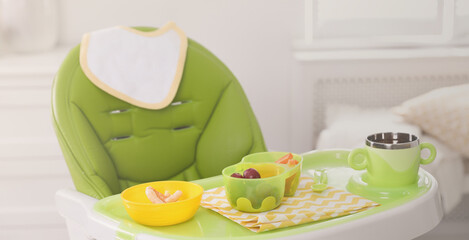 High chair with food in baby tableware on tray indoors. Banner design