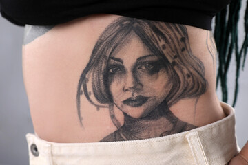Woman with tattoos on body against grey background, closeup