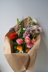 Large colored bouquet of different flowers in kraft packaging on a light background. Gift of expensive fresh flowers