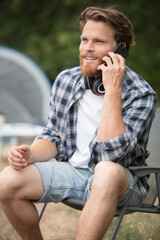 handsome cheerful man camping outdoors using mobile phone