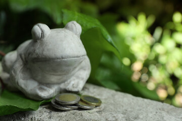 Frog figure with coins on stone parapet outdoors, closeup. Space for text