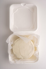 Small cake with cream without decor on a white background in a white package for delivery. Empty white cake top view