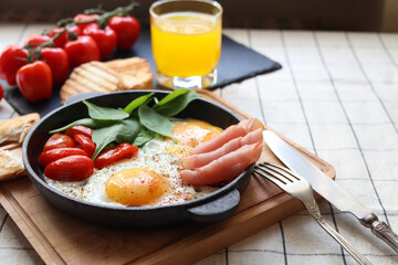 Delicious fried eggs with spinach, tomatoes and ham served on table