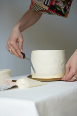 Confectioner's hands flatten white cream on a flat cake