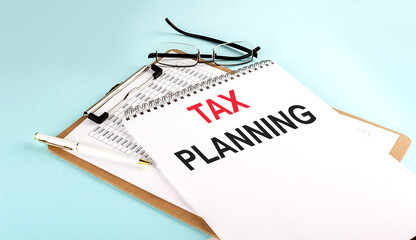 TAX PLANNING text on notepad on clipboard with chart on blue background, concept closeup. Business and finance concept