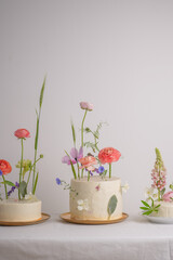Three beautiful white cakes with cream and fresh flowers on a white background and a white table with space for text