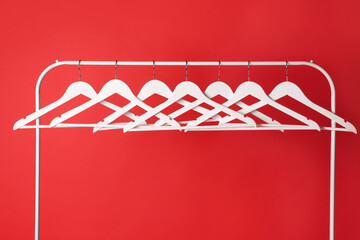 White clothes hangers on metal rack against red background