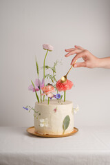Original cake decorated with flowers with a hand reaching for it a golden spoon on a white background