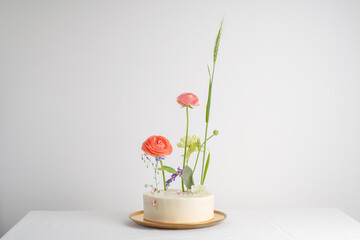 Perfect luxury white wedding cake with fresh flowers decor with pink ranunculus and leaf in light background, with space for text