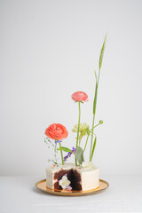 White cake with ranunculus with a chocolate cut on a golden plate on a white table