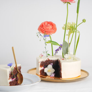 Original unique small vegan chocolate wedding cake with flowers on a white background in section with a plate and a portion of cake