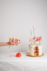 Female hand holding a piece of cake with pink and white cream near a beautiful cake on a white table