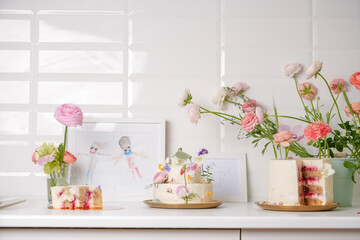 Bright creative cakes with fresh flowers decorated on the table in the home kitchen with white tiles