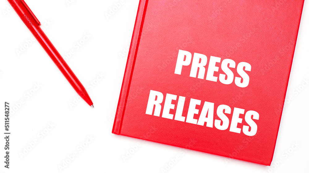 Poster the text press releases is written on a red notepad near a red pen on a white table in the office. b