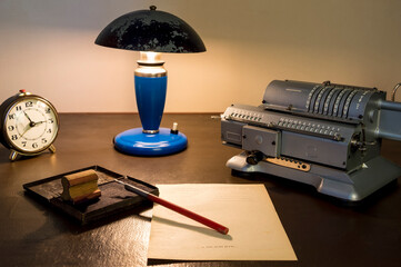 An old mechanical calculator, an antique table lamp, a pen and a stamp are office tools of the past.