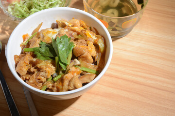 teriyaki chicken rice in white ceramic bowl with soup and salad on wood table with blank space on right corner