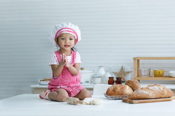 Cute little chef sitting on the table learning to make bread