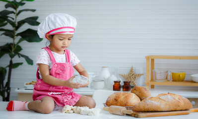 Cute little chef sitting on the table learning to make bread