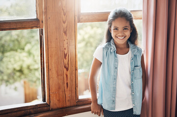 Happy kids make happy homes. Portrait of a happy young girl standing next to a window at home.