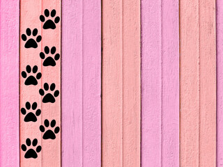 Black animal paw prints trail on a pink wooden background.