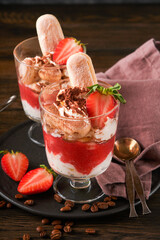 Strawberry tiramisu. Traditional Italian dessert tiramisu in glass with fresh strawberry and mint leaves on old wooden dark table background. Copy space. Food background.