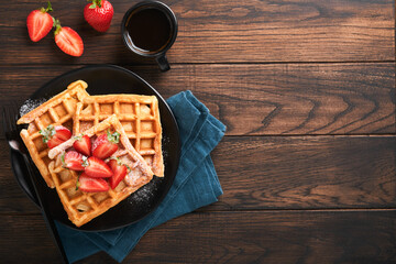Belgium waffles. Homemade waffles with strawberries, powdered sugar and cup of coffee on black plate on old wooden table background. Breakfast. Top view. Mockup for design idea.