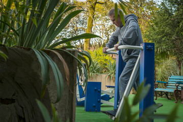 An elderly gray-haired man pensioner in a gray suit is training on simulators on a sports field on the street. The concept of an active healthy lifestyle of elderly pensioners.