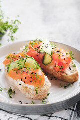 Sandwiches. Salmon toast with cream cheese, cucumber, black sesame and microgreens on gray concrete table background. Seafood. Healthy food. Top view.